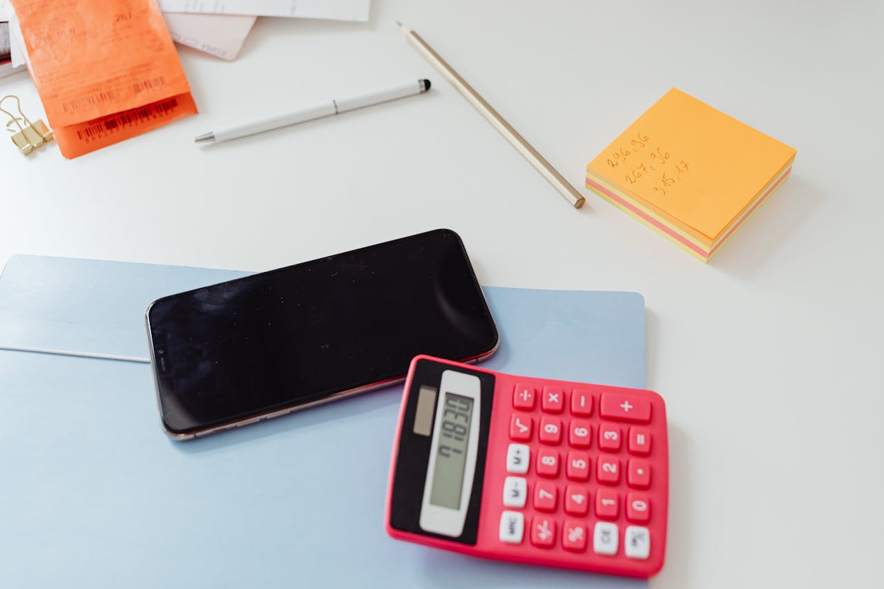 An organized office desk featuring a calculator, smartphone, and sticky notes on a white surface.